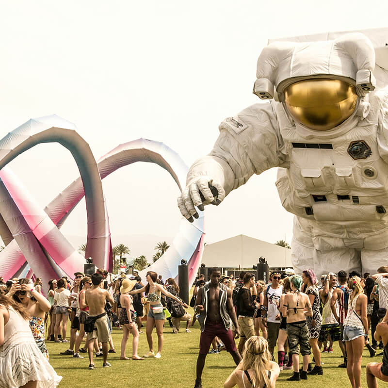 Coachella festival with astronaut statue and crowd.